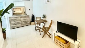 A modern living room with a flat-screen TV, wooden dining table, and chairs.