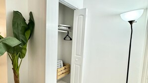 A hallway with a potted plant, a white door leading to a closet, and a standing floor lamp.