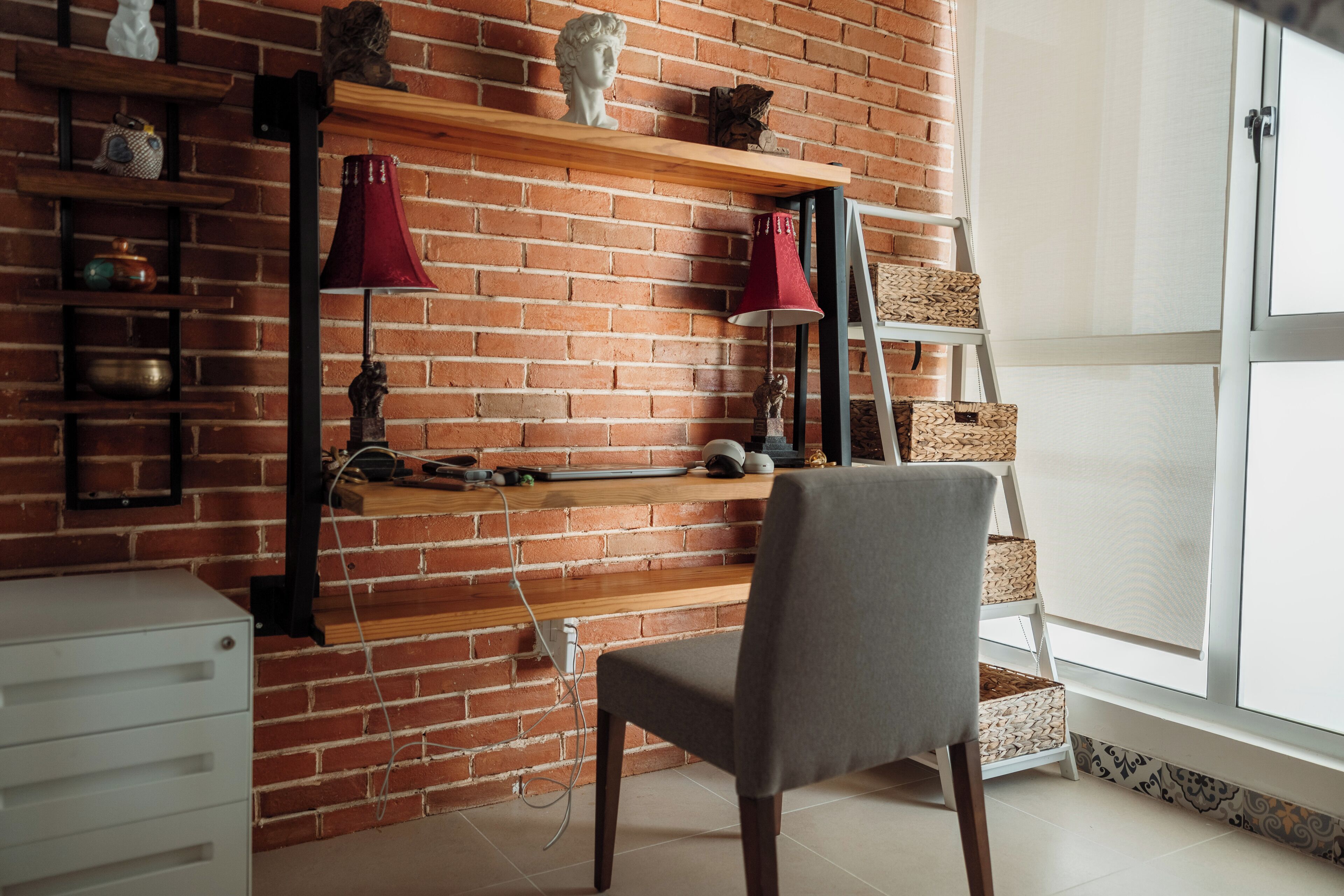 Ein Zimmer mit Backsteinwand, Holzregalen, einem Schreibtisch, einem Stuhl und einem Fenster.