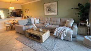Ein Wohnzimmer mit einem beigen Ecksofa, einem Holztisch und einem Essbereich im Hintergrund.