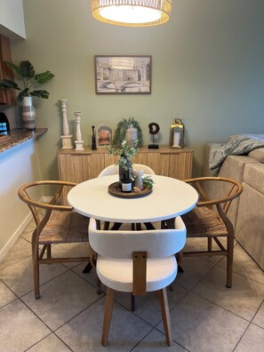 Un coin repas avec une table ronde, deux chaises, un vase avec des plantes, un tableau encadré au mur et une lampe suspendue au-dessus.