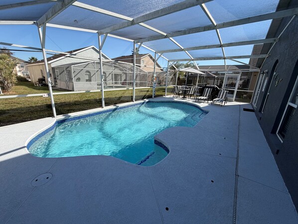Una piscina con cerramiento de vidrio, rodeada por una terraza con mobiliario exterior.