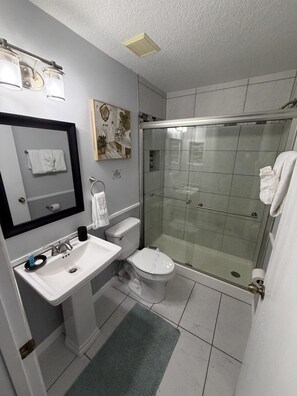 Un baño moderno con ducha de vidrio, un lavamanos blanco y un inodoro.