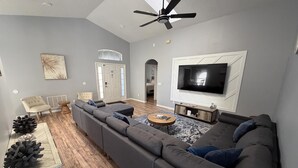 A modern living room with a sectional sofa, a flat-screen TV, and a ceiling fan. - Beautiful Hampton Lakes Home - RECENTLY RENOVATED (Davenport)