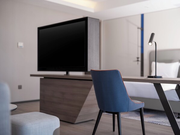 A modern hotel room with a flat-screen TV, a desk with a lamp, a blue chair, and a bed with white bedding. - Holiday Inn Express Wuxi Taihu by IHG (Wuxi)