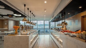 Un hall d’hôtel moderne avec des comptoirs en marbre, un espace buffet et de grandes fenêtres offrant une vue sur la ville.