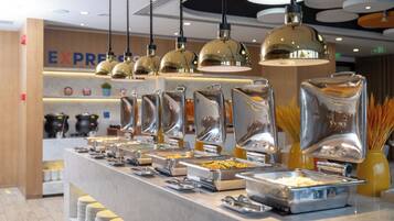 A buffet area with multiple food stations, stainless steel serving trays, and hanging pendant lights.