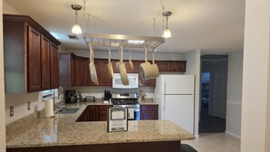 A kitchen with granite countertops, wooden cabinets, a stainless steel refrigerator, and hanging pots. - Family Times Cabin (Sevierville)