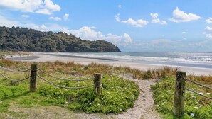 Un camino costero que lleva a una playa, con una valla de madera y vegetación.