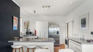 Una cocina moderna con una isla central, taburetes blancos de bar, electrodomésticos de acero inoxidable y una pared de acento negra.