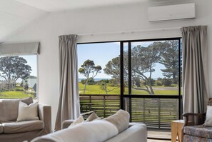 A modern living room with a large window offering a view of a grassy area and trees.