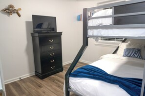 A bunk bed with white bedding and a blue blanket, a black dresser with gold handles, and a wall-mounted fish decoration. - Cozy Home Away From Home (Woodbridge)