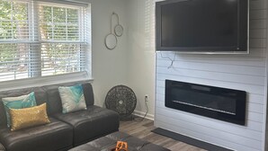 Una sala de estar moderna con un sofá modular, un televisor de pantalla plana montado en una pared blanca y una chimenea debajo.