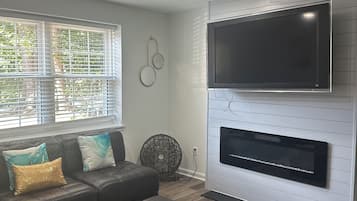 A modern living room with a sectional sofa, a flat-screen TV mounted on a white wall, and a fireplace below it.