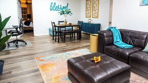 Una sala de estar moderna con un sofá de cuero, una mesa de comedor con sillas, un florero con flores y una decoración de pared con la palabra 'blessed'.