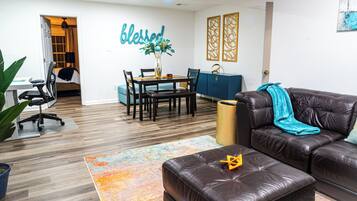 A modern living room with a leather couch, a dining table with chairs, a vase with flowers, and a 'blessed' wall decoration.