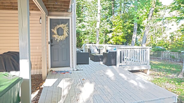 Una terraza de madera con mobiliario exterior, una puerta adornada con una corona y un patio cercado.