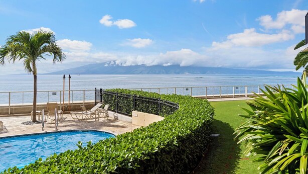 Ein Poolbereich mit Liegestühlen, einer Palme und Blick auf das Meer und die Berge.