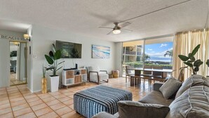 Ein geräumiges Wohnzimmer mit einer großen Couch, einem Couchtisch und einem Fernseher. Ein Balkon bietet Blick auf den Ozean.