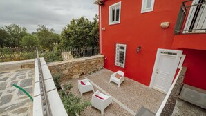 A red building with a stone wall, a white door, and a small balcony with white chairs and a table. - Lagarteiro House (Porto)