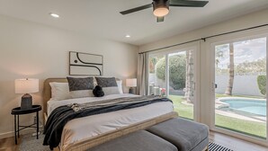 Un dormitorio con cama, mesitas de noche, ventilador de techo y vista a una piscina.