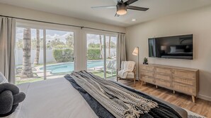 Un dormitorio con una cama grande, televisión, ventilador de techo y vista a una piscina.