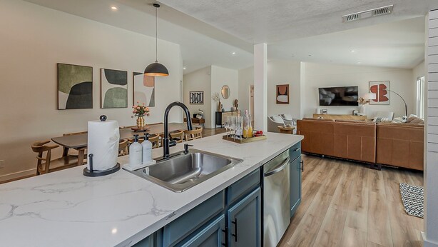 A modern kitchen with a marble countertop, stainless steel sink, and a dining area with wooden chairs.