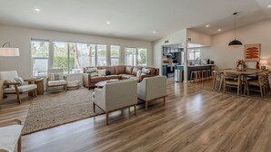 A spacious living room with a large brown leather sofa, a dining area with a wooden table and chairs, and a kitchen in the background.
