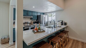 Una cocina moderna con gabinetes color turquesa, encimera blanca y una barra con taburetes.