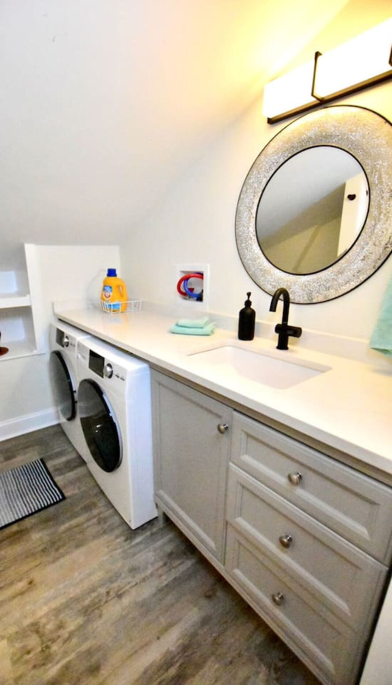 A compact laundry room with a washing machine, a sink, and a mirror.