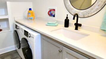 A compact laundry room with a washing machine, a sink, and a mirror.