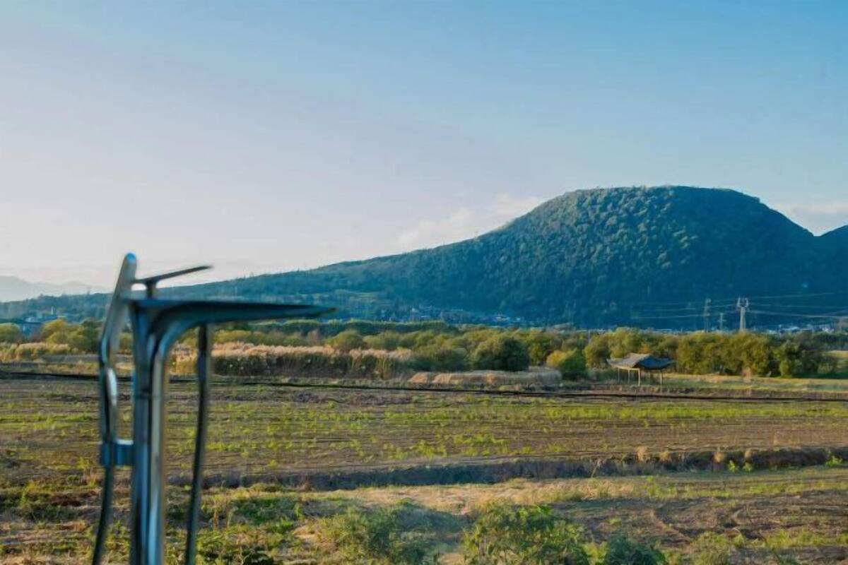 Paisagem rural com uma estrutura metálica em primeiro plano, uma montanha ao fundo e campos.