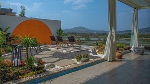 A rooftop terrace with a pool, lounge chairs, and a view of a distant landscape.