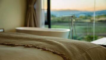 Una cama con una manta texturizada, una ventana con vistas a un paisaje y un inodoro al fondo.