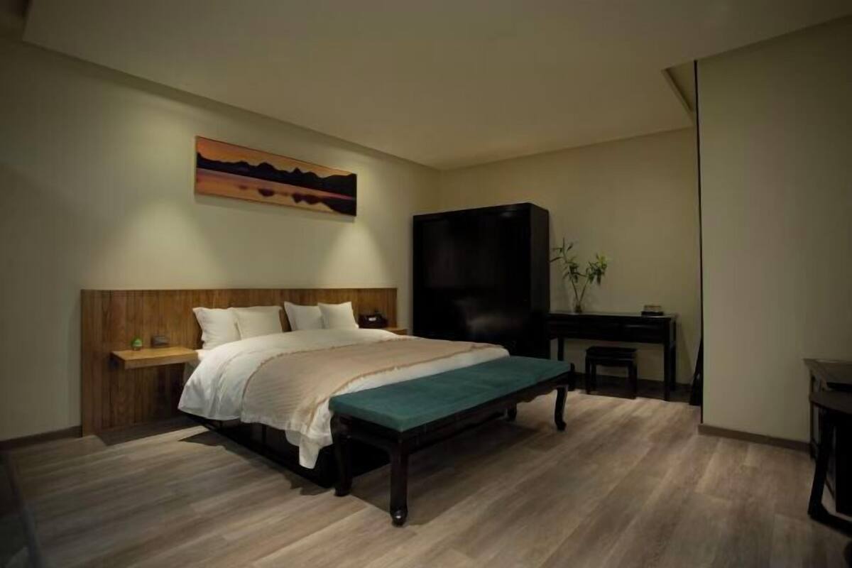 Quarto com uma cama, um banco, uma escrivaninha e uma televisão.