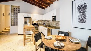A modern kitchen with white cabinets, stainless steel appliances, and a wooden dining table set for four. - Casa Piña - Tamarindo 5 min Walk to Beach (Tamarindo)