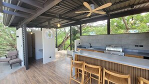 A modern kitchen with a bar area, wooden stools, and a ceiling fan. - Casa Piña - Tamarindo 5 min Walk to Beach (Tamarindo)