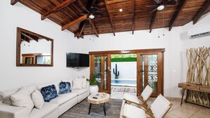 A living room with a white sofa, a coffee table, and two wicker chairs. There is a TV mounted on the wall, a ceiling fan, and a wooden ceiling. - Casa Piña - Tamarindo 5 min Walk to Beach (Tamarindo)
