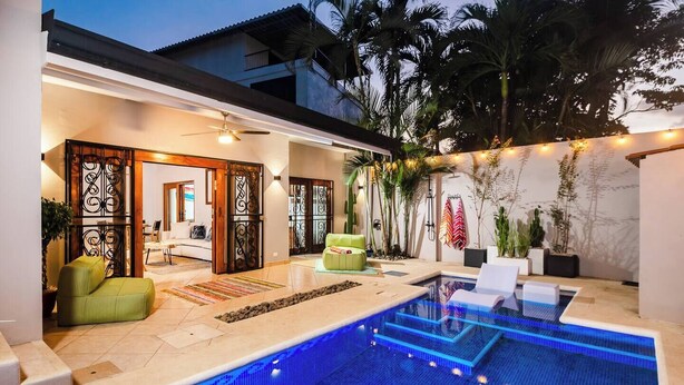 A modern outdoor pool area with a clear blue pool, a green sofa, and a white lounge chair. - Casa Piña - Tamarindo 5 min Walk to Beach (Tamarindo)