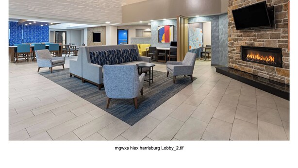 A lobby with a sofa, chairs, a fireplace, a TV, and a blue patterned wall.
