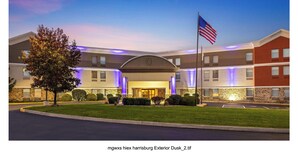 A modern hotel exterior with a well-lit entrance, a flag, and a landscaped lawn.