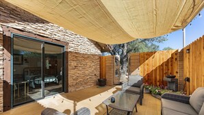 A covered patio area with wicker furniture, a stone wall, and a wooden fence. - French Countryside Villa at Dorner Family Vineyard (Tehachapi)