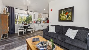 A modern living room with a grey sofa, a wooden coffee table, and a dining area with white furniture. - French Countryside Villa at Dorner Family Vineyard (Tehachapi)
