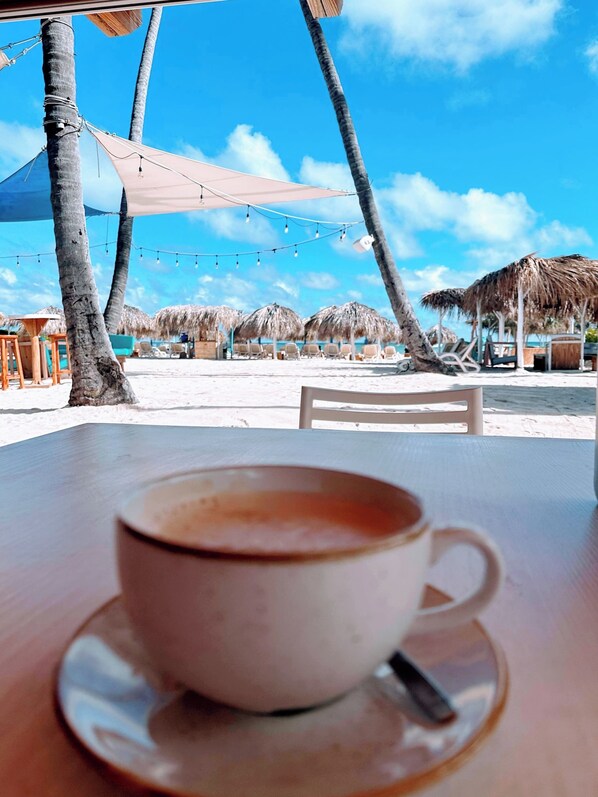 A cup of coffee on a table with a view of a beach and palm trees.