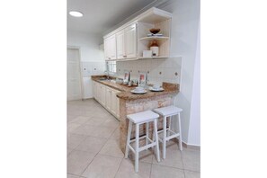 A kitchen with white cabinets, a granite countertop, and two white stools.