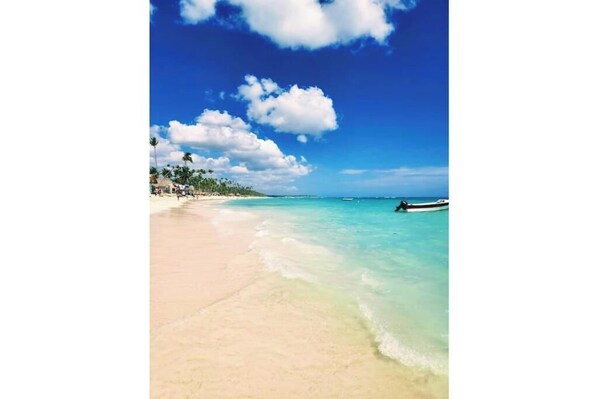 A beach with clear turquoise water, a sandy shore, and a small boat in the distance.