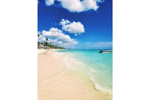 Ein Strand mit klarem türkisblauem Wasser, einem Sandufer und einem Boot in der Ferne.