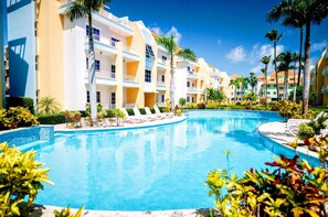 A resort with a swimming pool, multiple-story buildings, and palm trees.