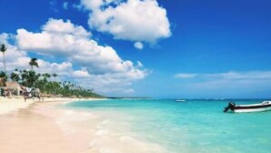 A beach with clear turquoise water, a sandy shore, and a small boat in the distance.