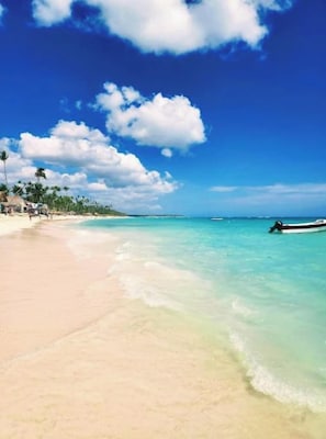 A beach with clear turquoise water, a sandy shore, and a small boat in the distance.